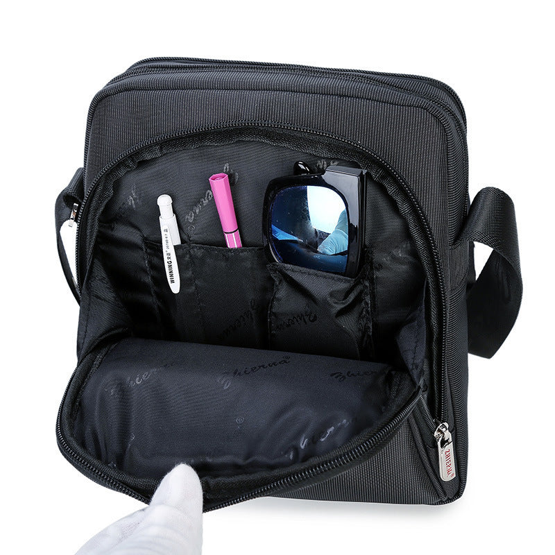 Black crossbody bag with compartments containing a phone, sunglasses, and makeup items on a white background.