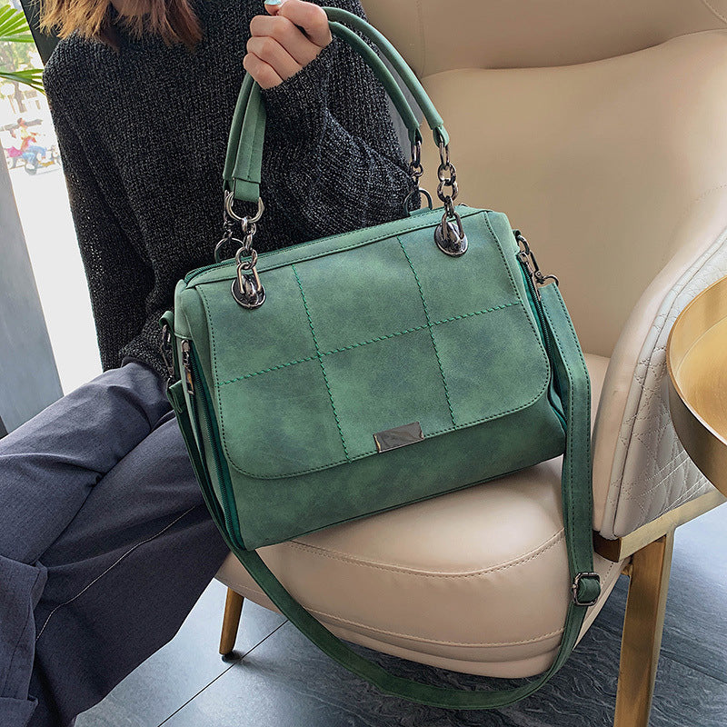 Green handbag held by a person sitting on a beige chair.