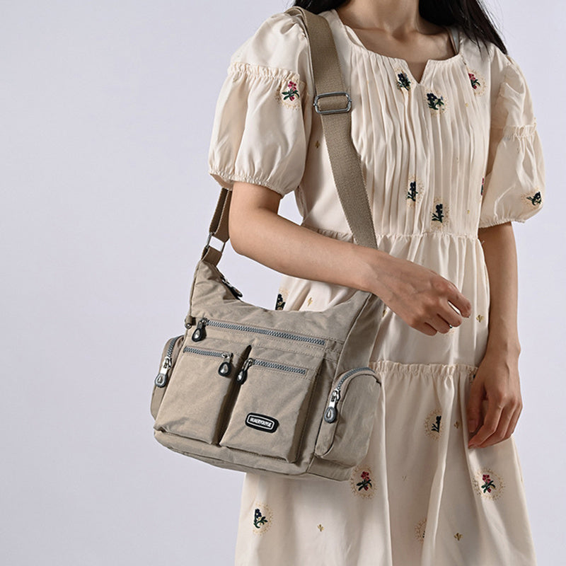 Woman wearing a beige dress with floral embroidery, carrying a beige shoulder bag against a light gray background