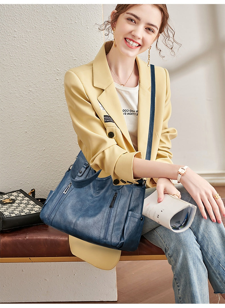 Woman sitting on a bench wearing a yellow blazer and blue jeans, holding a blue handbag.
