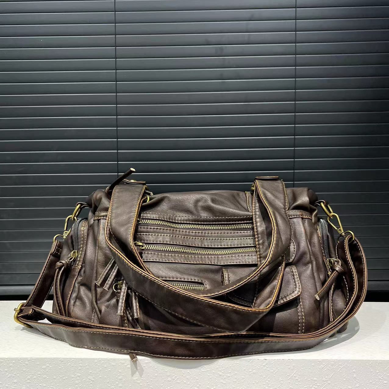 Brown leather handbag with multiple zippers on a gray surface and black background