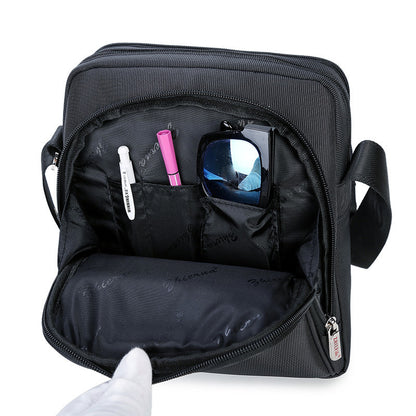 Black crossbody bag with compartments containing a phone, sunglasses, and makeup items on a white background.