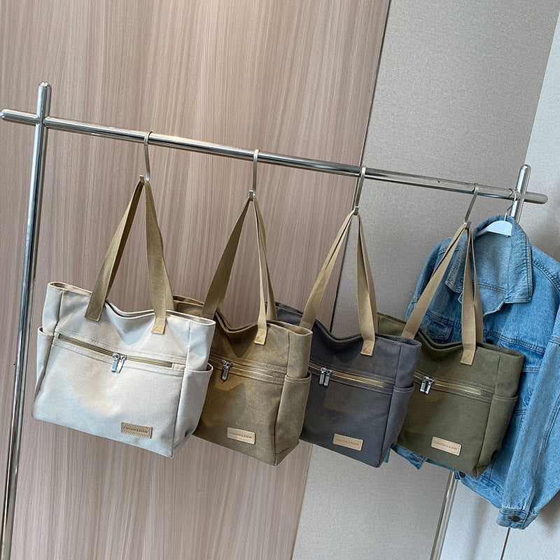 Four handbags of different colors hanging on a rack against a neutral wall.