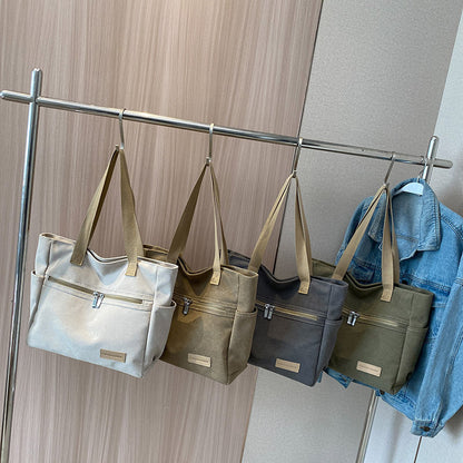 Four handbags of different colors hanging on a rack against a neutral wall.