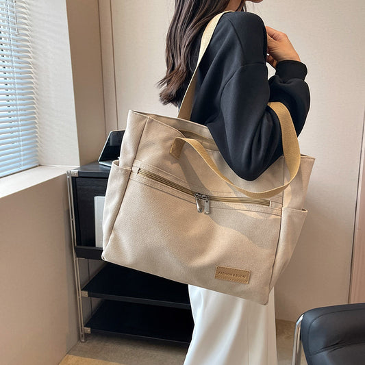 Person holding a beige tote bag with a visible brand logo in an indoor setting.