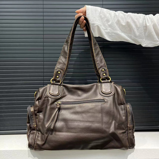 Brown leather handbag held by a person against a neutral background