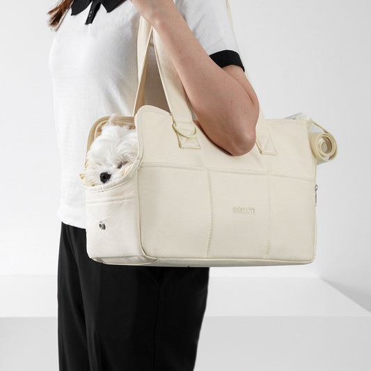 Person holding a beige pet carrier with a small dog inside on a white background