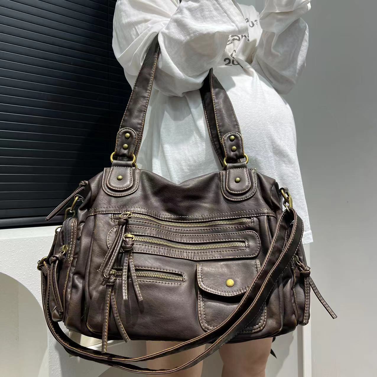 Brown leather handbag with multiple pockets and straps held by a person wearing a white shirt.