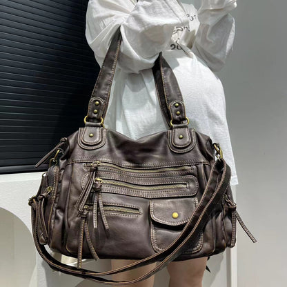 Brown leather handbag with multiple pockets and straps held by a person wearing a white shirt.