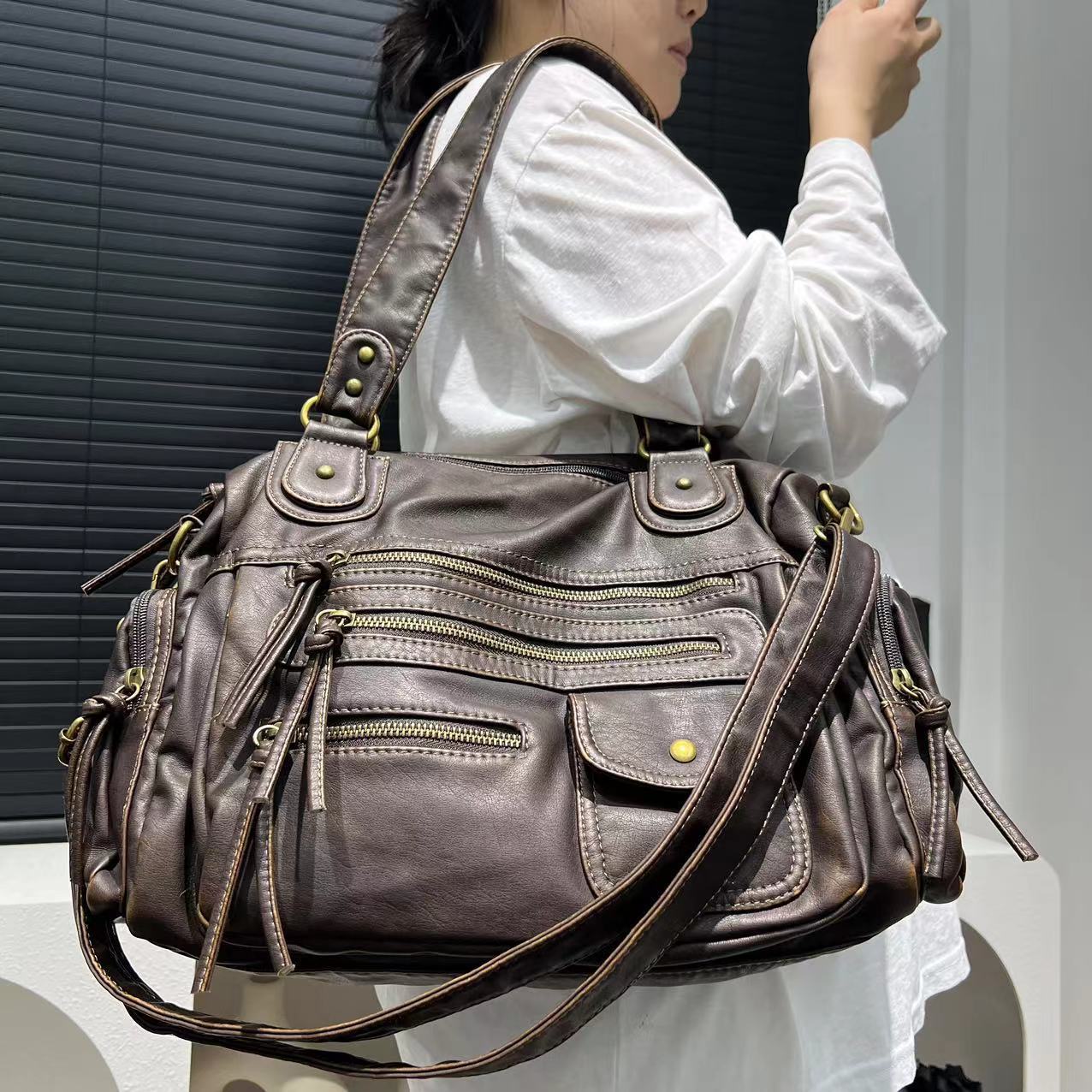 Person holding a large brown leather handbag with multiple zippers.