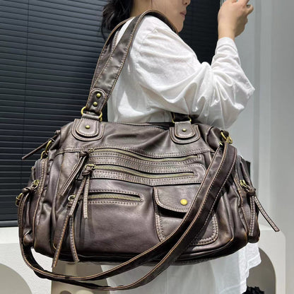 Person holding a large brown leather handbag with multiple zippers.