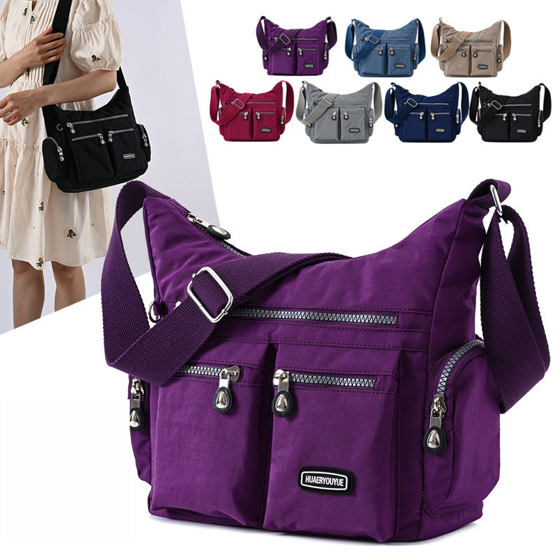 Purple shoulder bag with multiple pockets and zippers, displayed with other color options in the background.