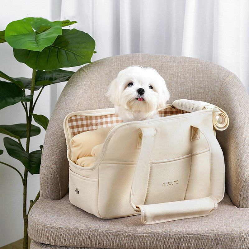 White dog sitting inside a beige pet carrier on a chair with a plant in the background
