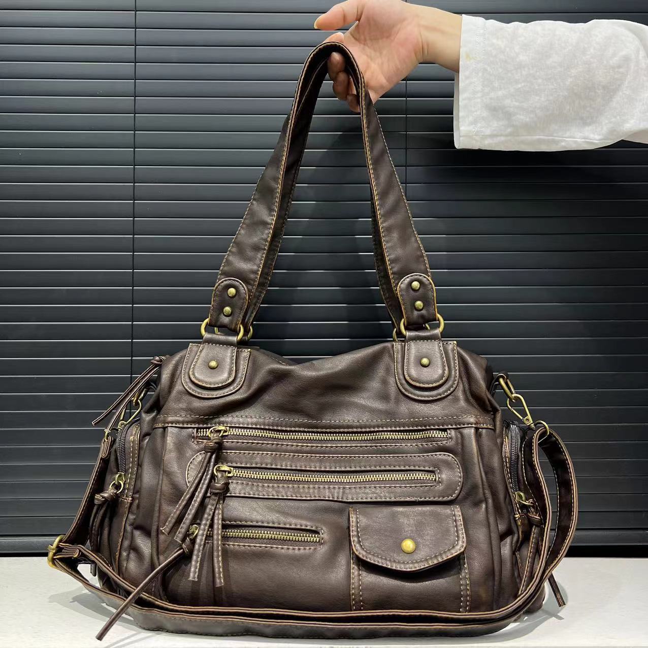 Brown leather handbag with gold hardware held by a person against a dark background