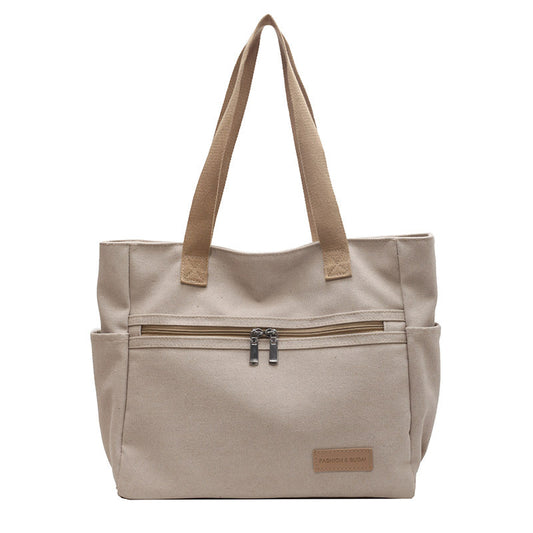 Beige tote bag with brown handles and zippers on a white background