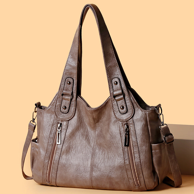 Brown leather handbag with multiple pockets and zippers on a beige background