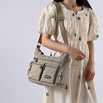 Woman wearing a beige dress with floral embroidery, carrying a beige shoulder bag against a light gray background