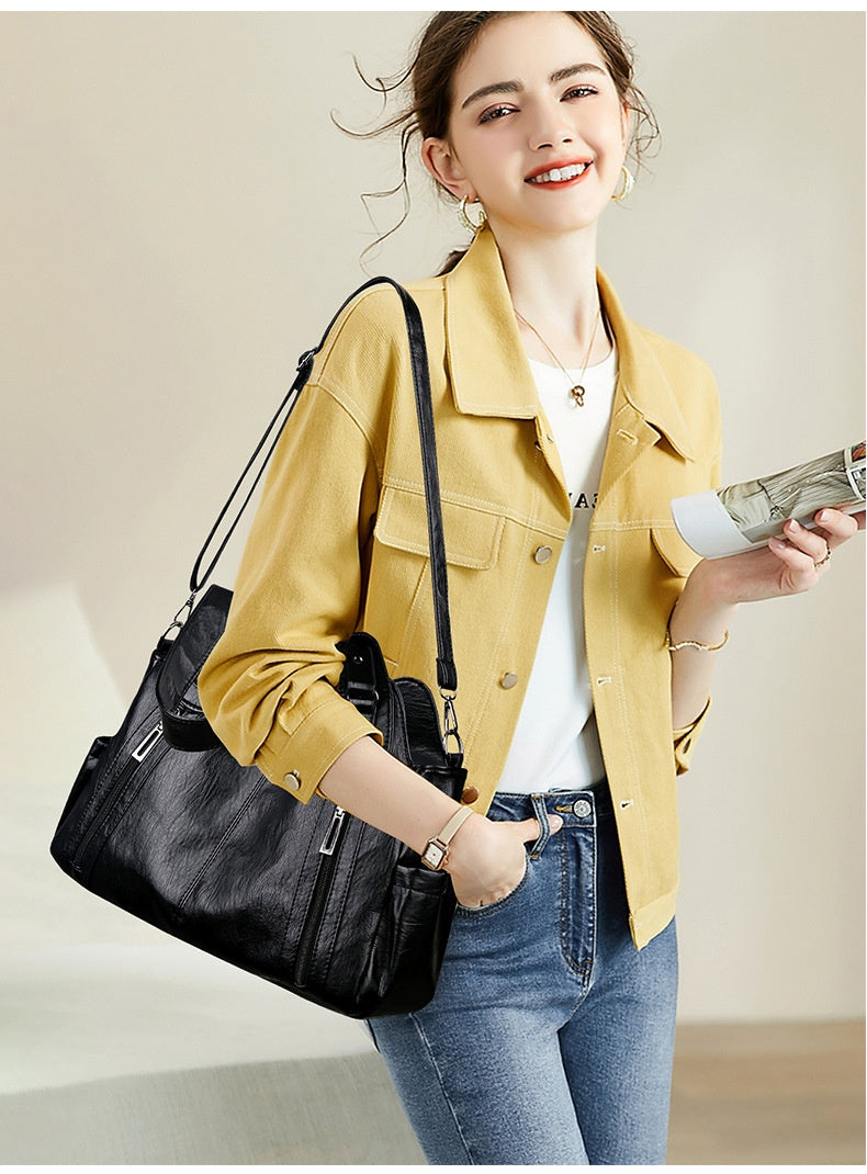 Woman in yellow jacket holding a black handbag and a phone on a neutral background