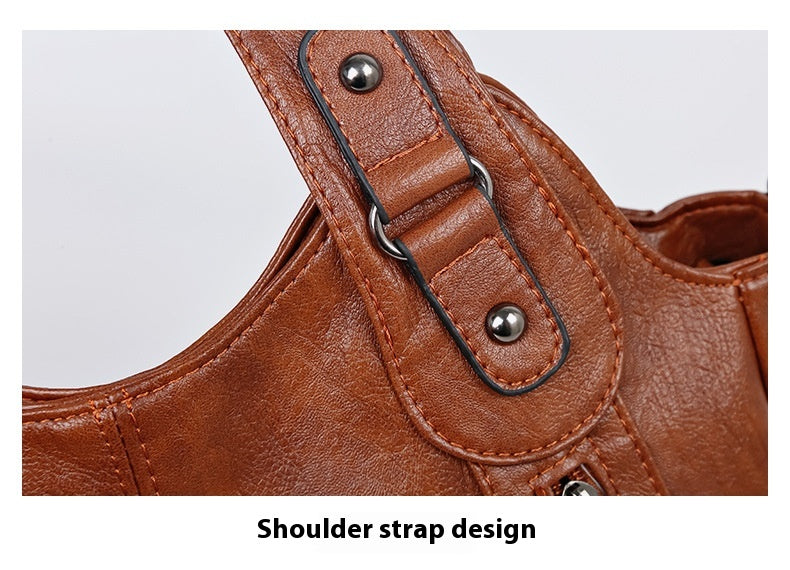 Close-up of a brown leather handbag with shoulder strap design on a light gray background.