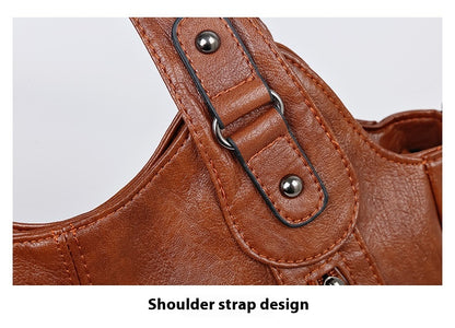 Close-up of a brown leather handbag with shoulder strap design on a light gray background.
