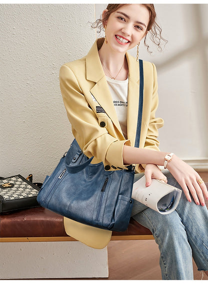 Woman sitting on a bench wearing a yellow blazer and blue jeans, holding a blue handbag.