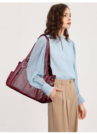Woman holding a large burgundy handbag against a plain background