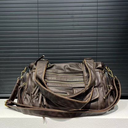 Brown leather handbag with multiple zippers on a gray surface and black background